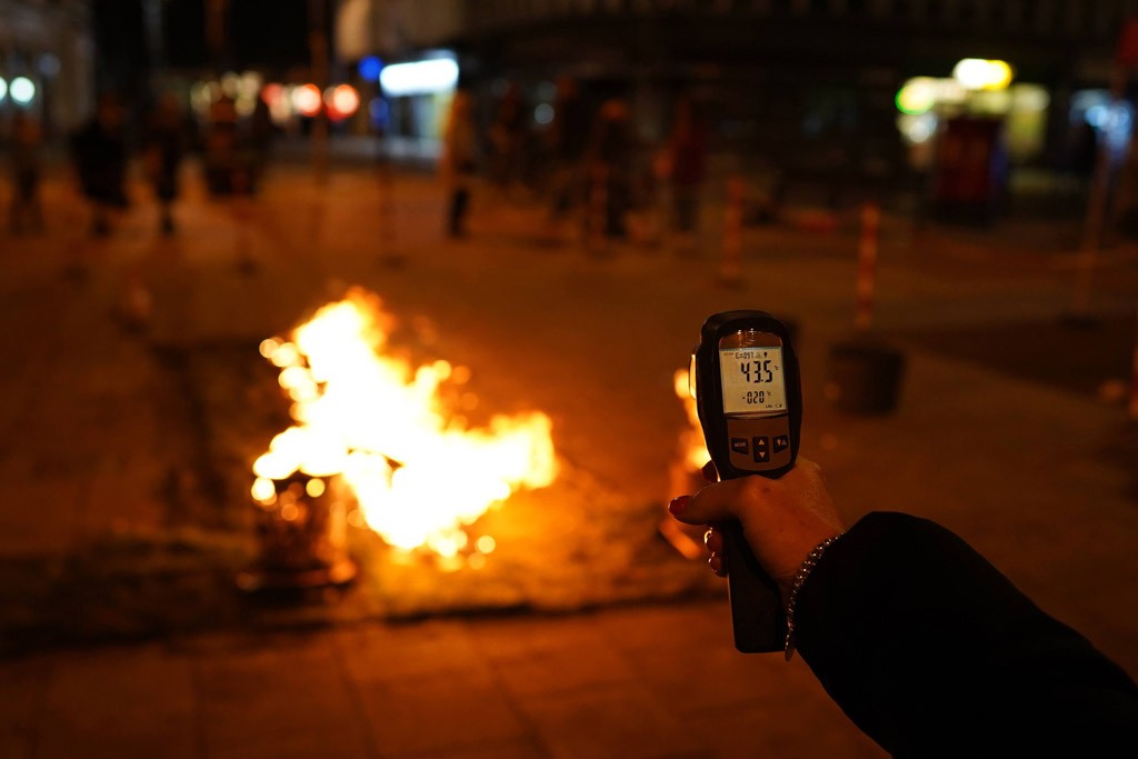 A hand holding an infared thermometer. It is directed towards the fire which is blurred in the background