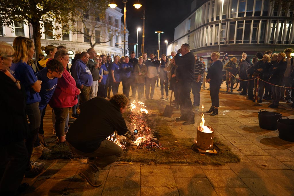 People gathered round the fire lane as it is prepared for the walk. An ETI team member is measuring the temperature of the fire using an infrared thermometer 