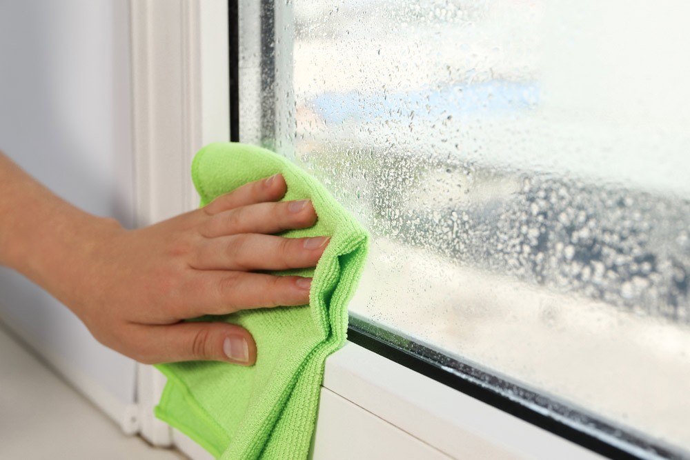 Hand wiping condensation from a window using a green microfibre cloth