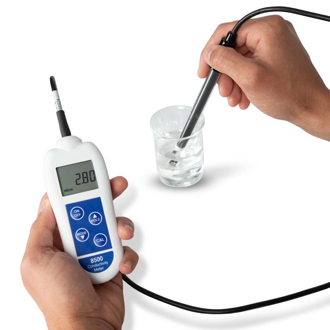 A person testing a beaker of water using the ETI 8500 Conductivity Meter