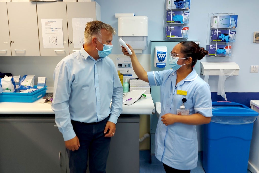 NHS nurse checks patient temperature using infrared forehead thermometer