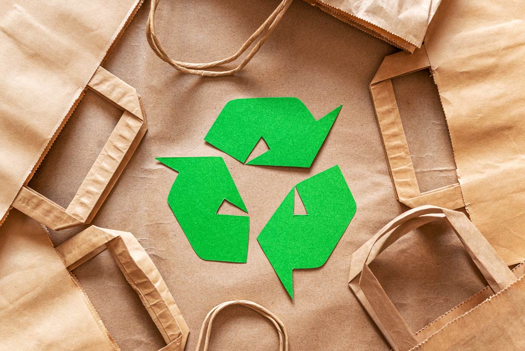 Green reduce, reuse, recycle arrows surrounded by brown paper bags.