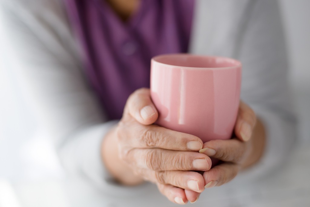 An older person holding a pink mug between their hands to warm them up