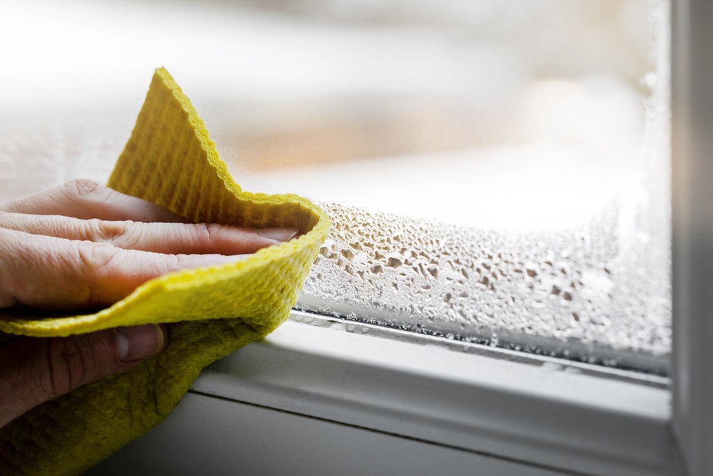 A person wiping condensation from a window using a yellow cloth